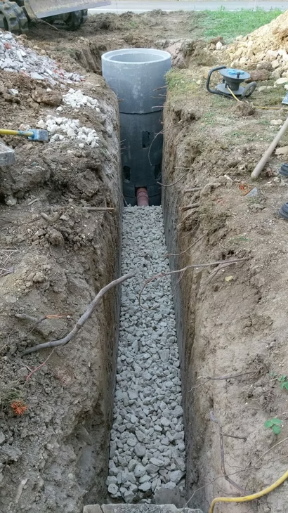 Tranchée avec drain en gravier menant à une fosse septique en plastique noir en construction à l'extérieur