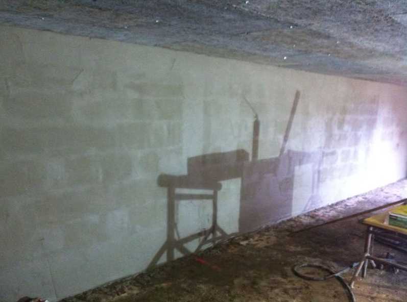 Mur en parpaings faiblement éclairé, avec l'ombre d'un établi et d'outils dans un espace ressemblant à un sous-sol