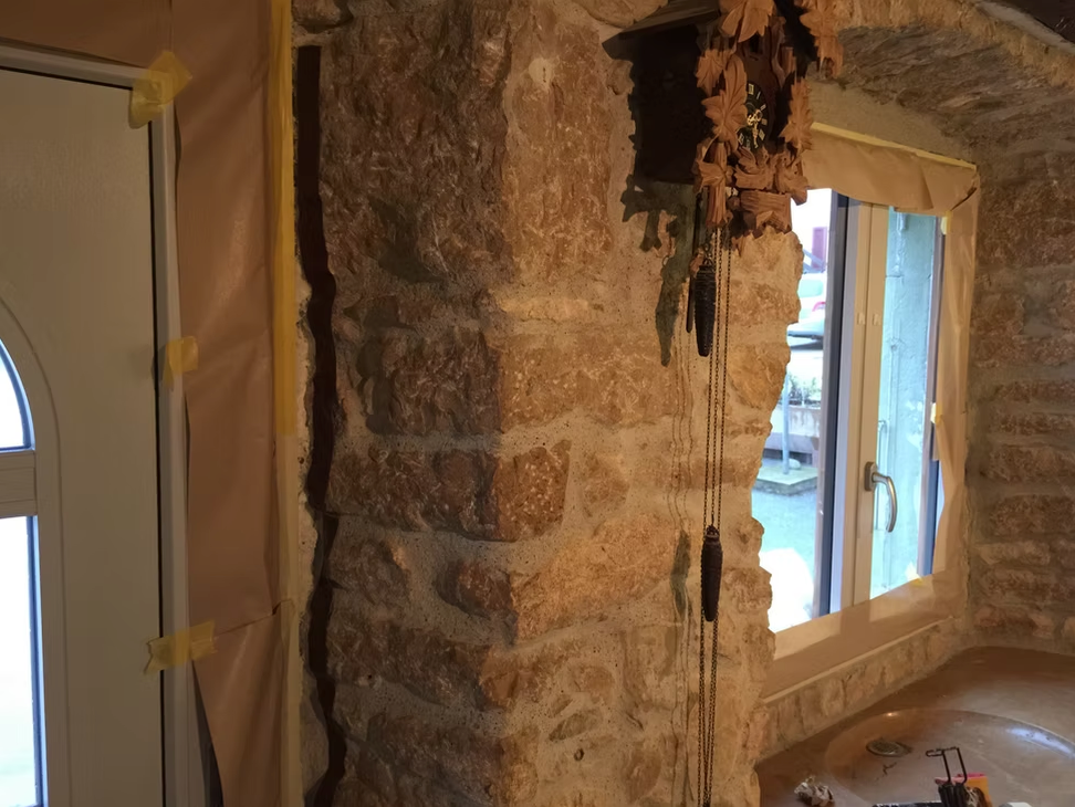 Mur intérieur en pierre avec une petite fenêtre et une porte, éclairé par la lumière du jour.