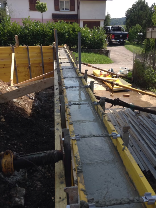 Chantier de construction avec une longue tranchée de fondation en béton à côté d'une maison, des coffrages en bois
