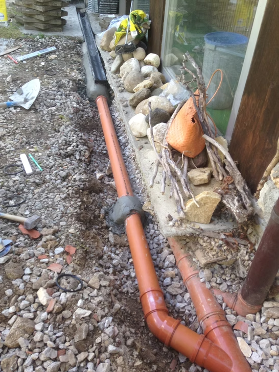 Tuyau de drainage orange et gravier le long d'un mur de bâtiment, avec des rochers et une bordure de jardinière.