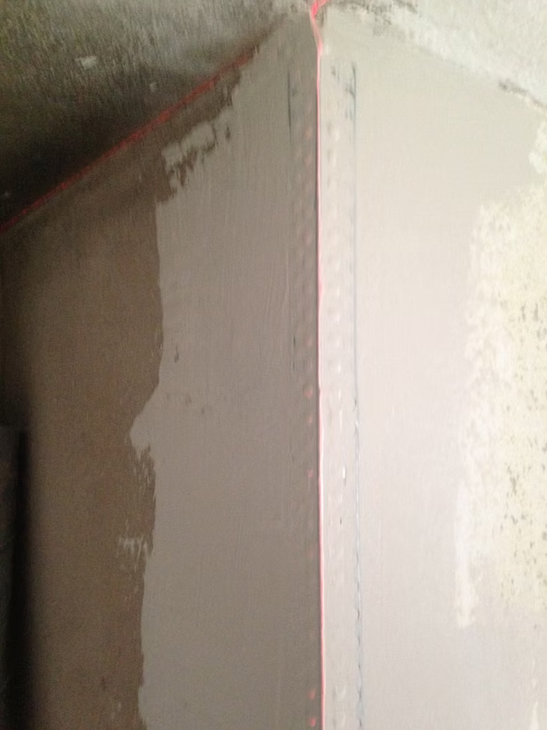 Mur d'angle partiellement peint avec apprêt gris et rebouchage de plâtre blanc