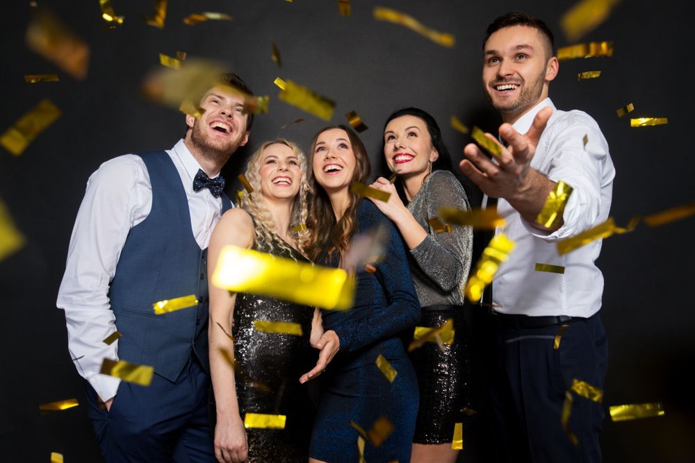 A group of people are standing in front of a wall with confetti falling around them.