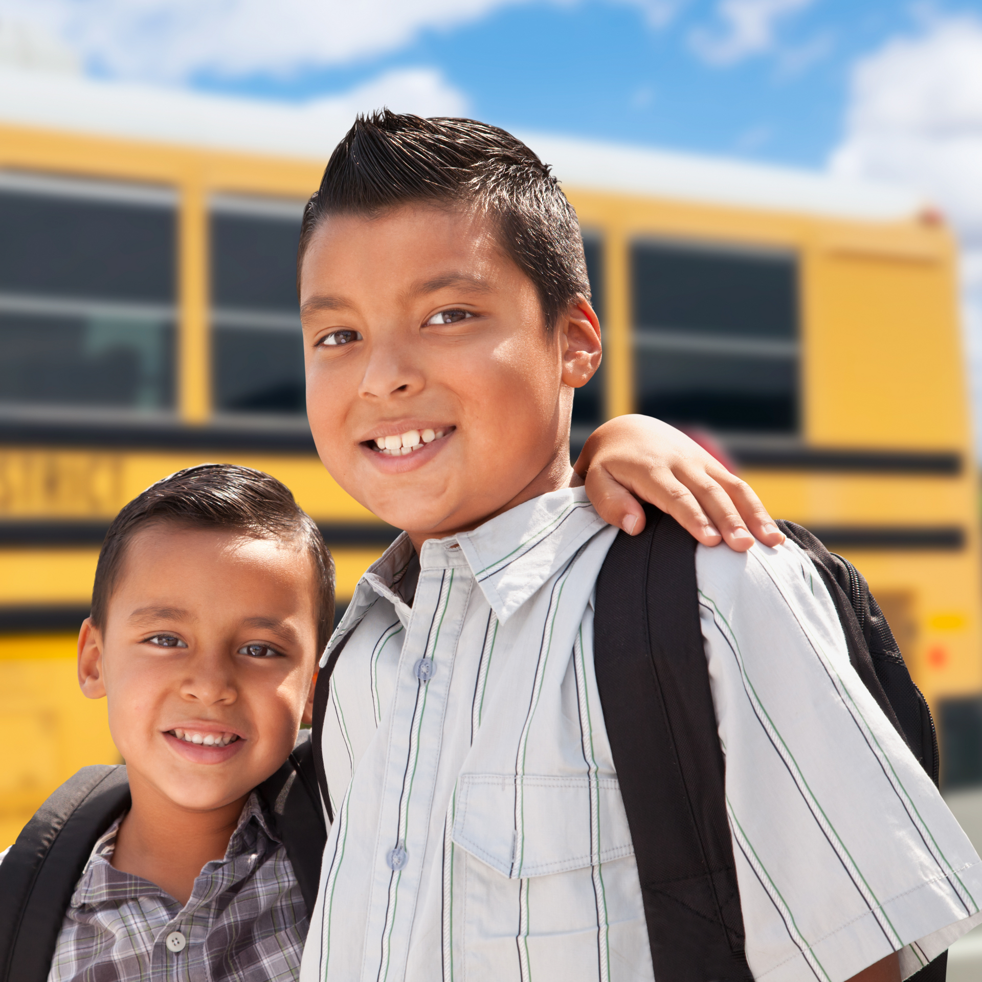 Two boys are posing for a picture in front of a school bus
