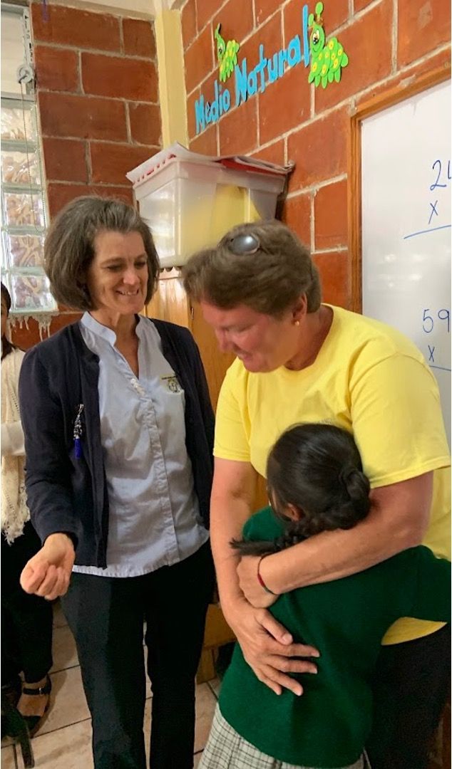 Donation Information A woman in a yellow shirt is hugging a child in a classroom.