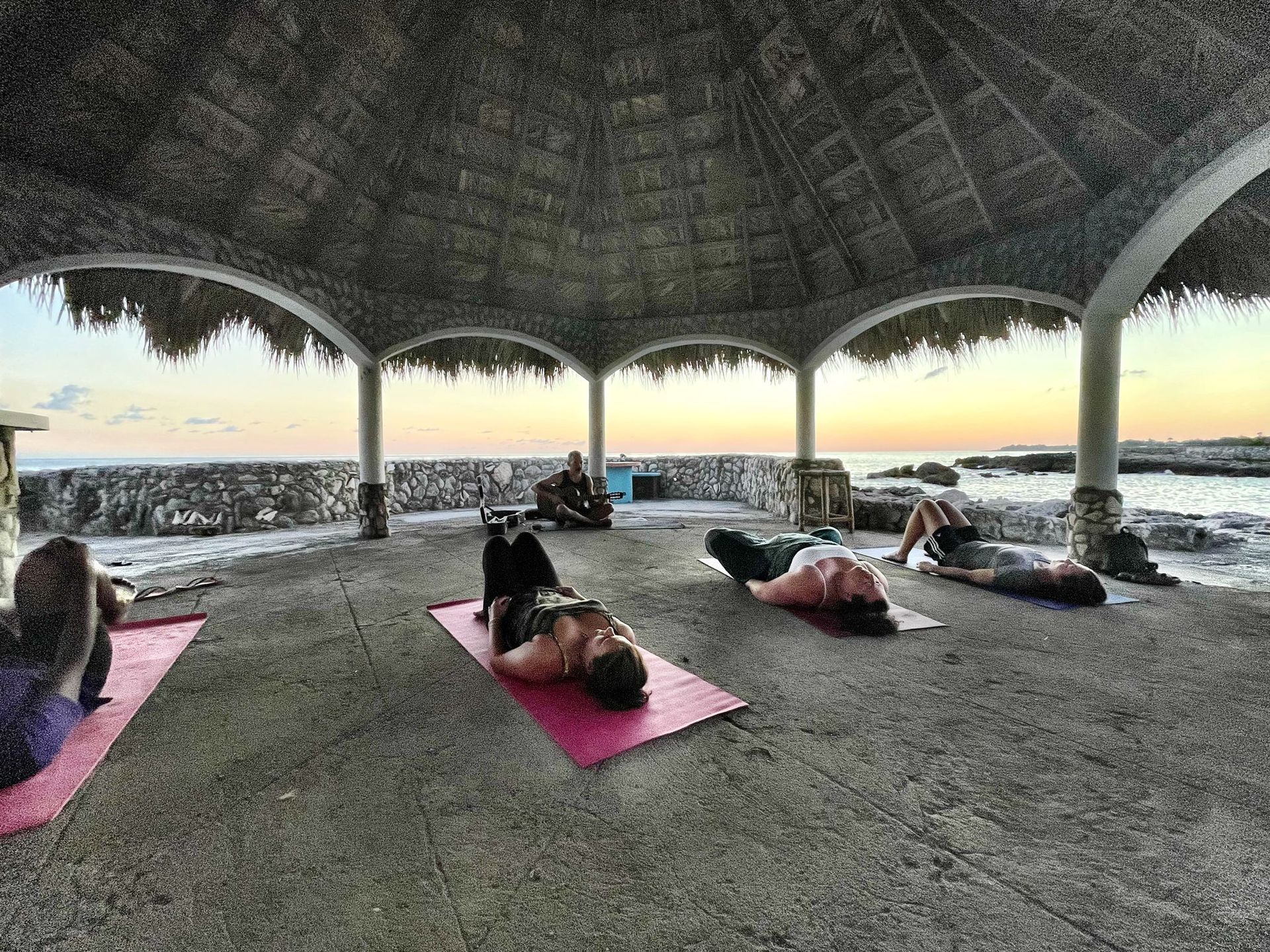 Guests practicing yoga in an open-air pavilion beside the sea