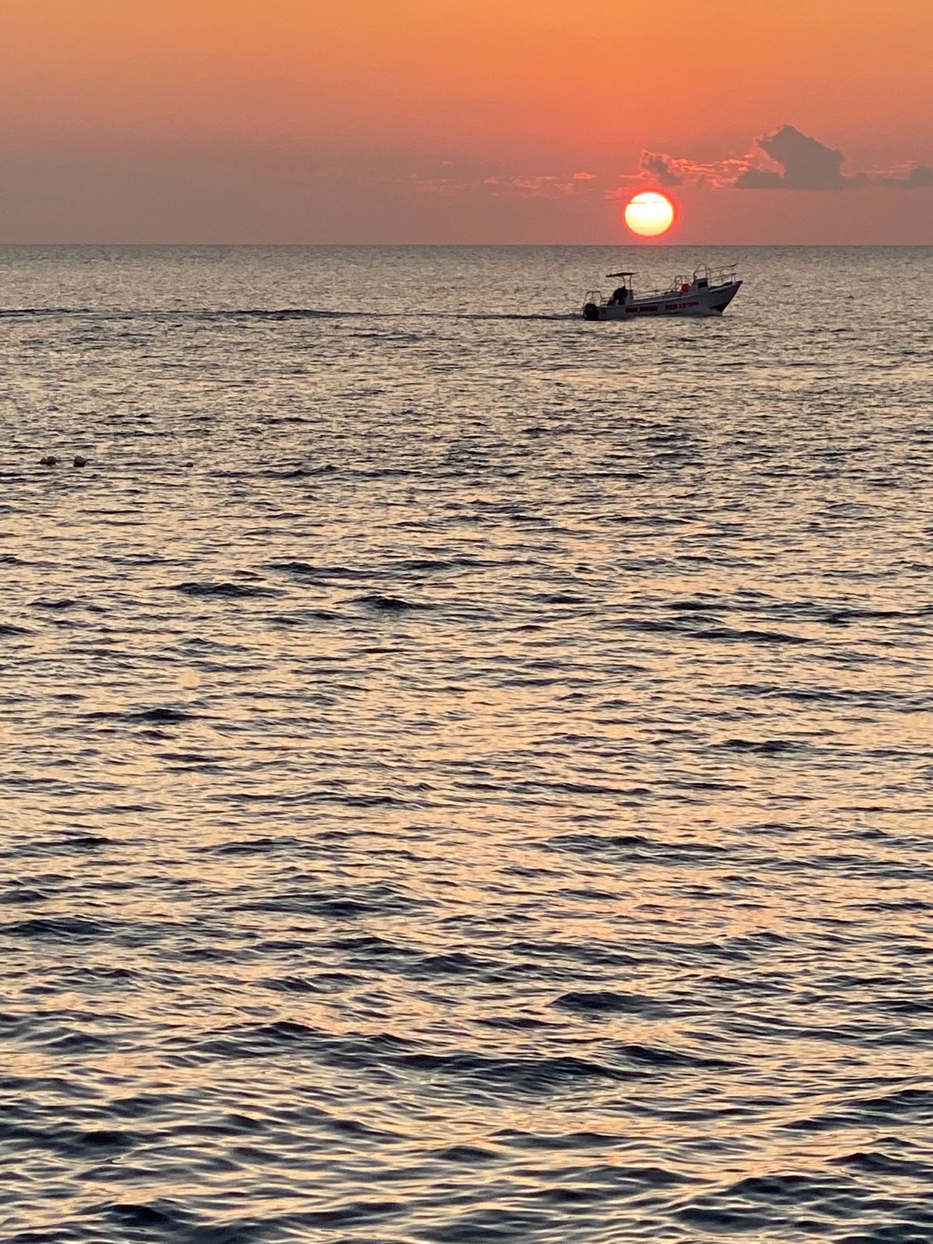 A boat floating offshore at sunset