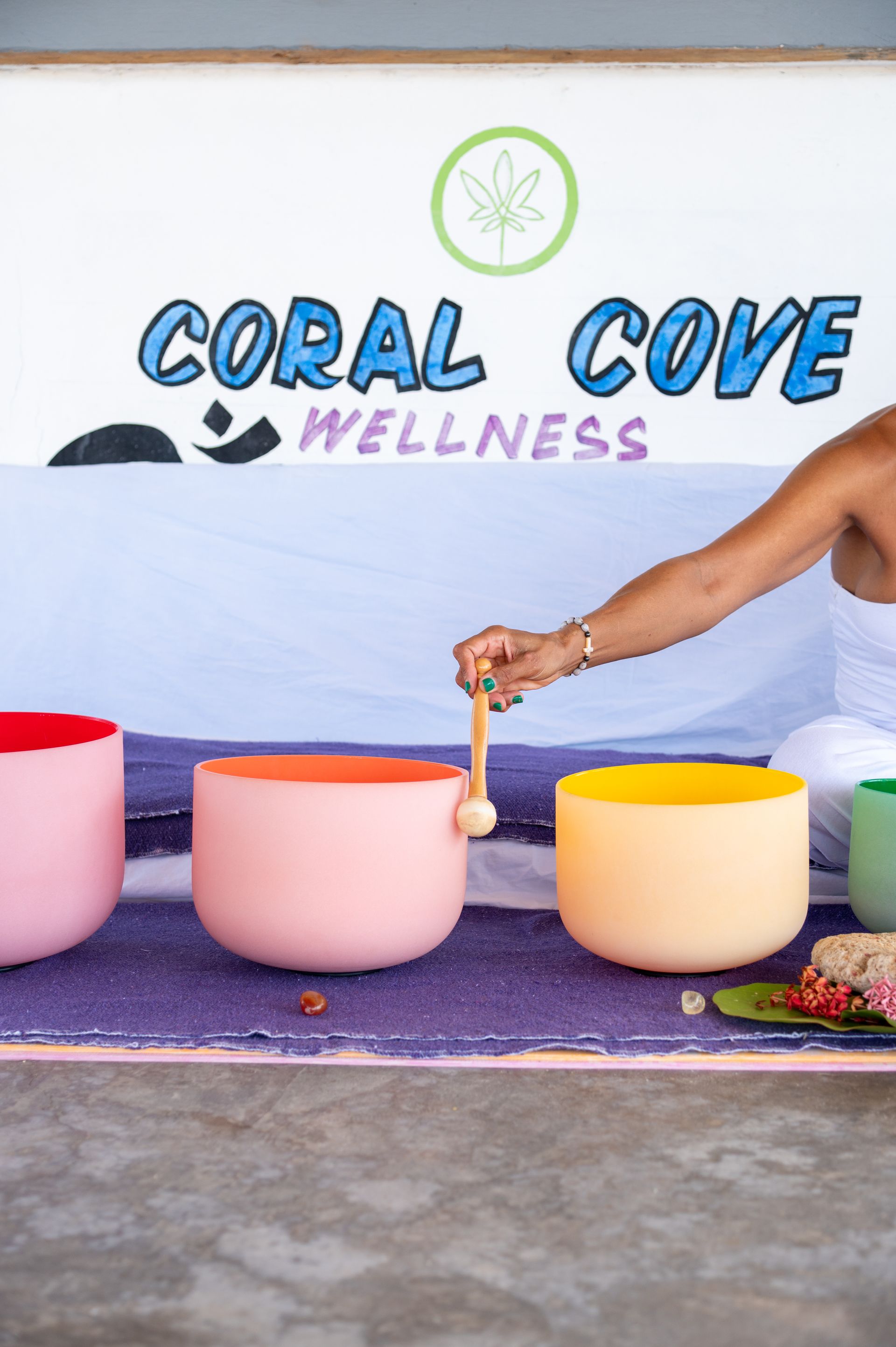 A woman is playing a sound bowl in front of a sign that says coral cove wellness.
