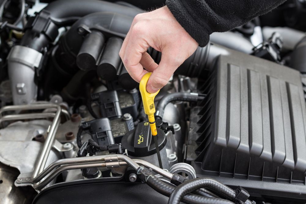Hand Pulling a Yellow Dipstick from A Car Engine to Check the Oil Level — Maryborough Exhaust & Mechanical In Maryborough, QLD