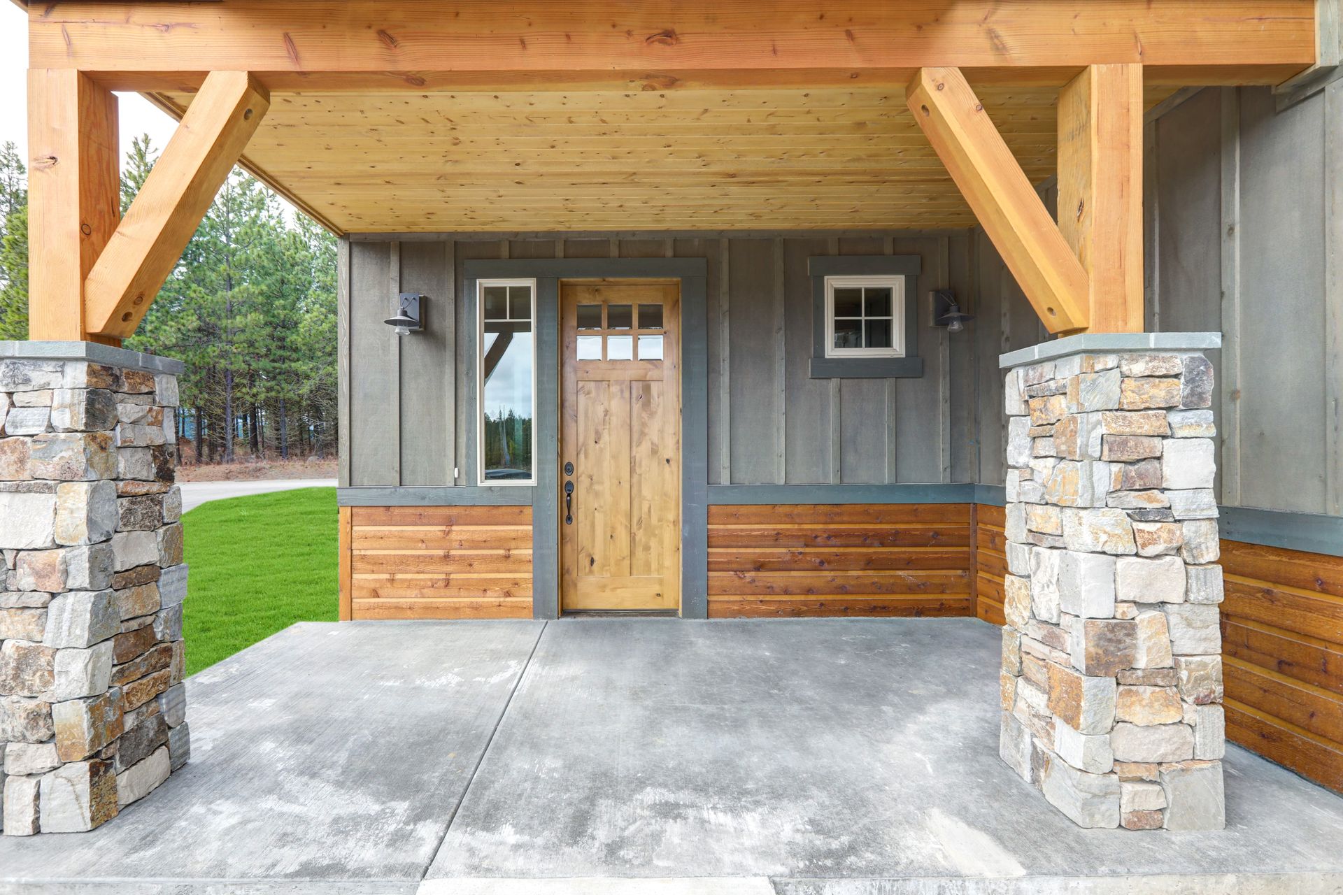 A rustic covered porch with a natural wood front door.