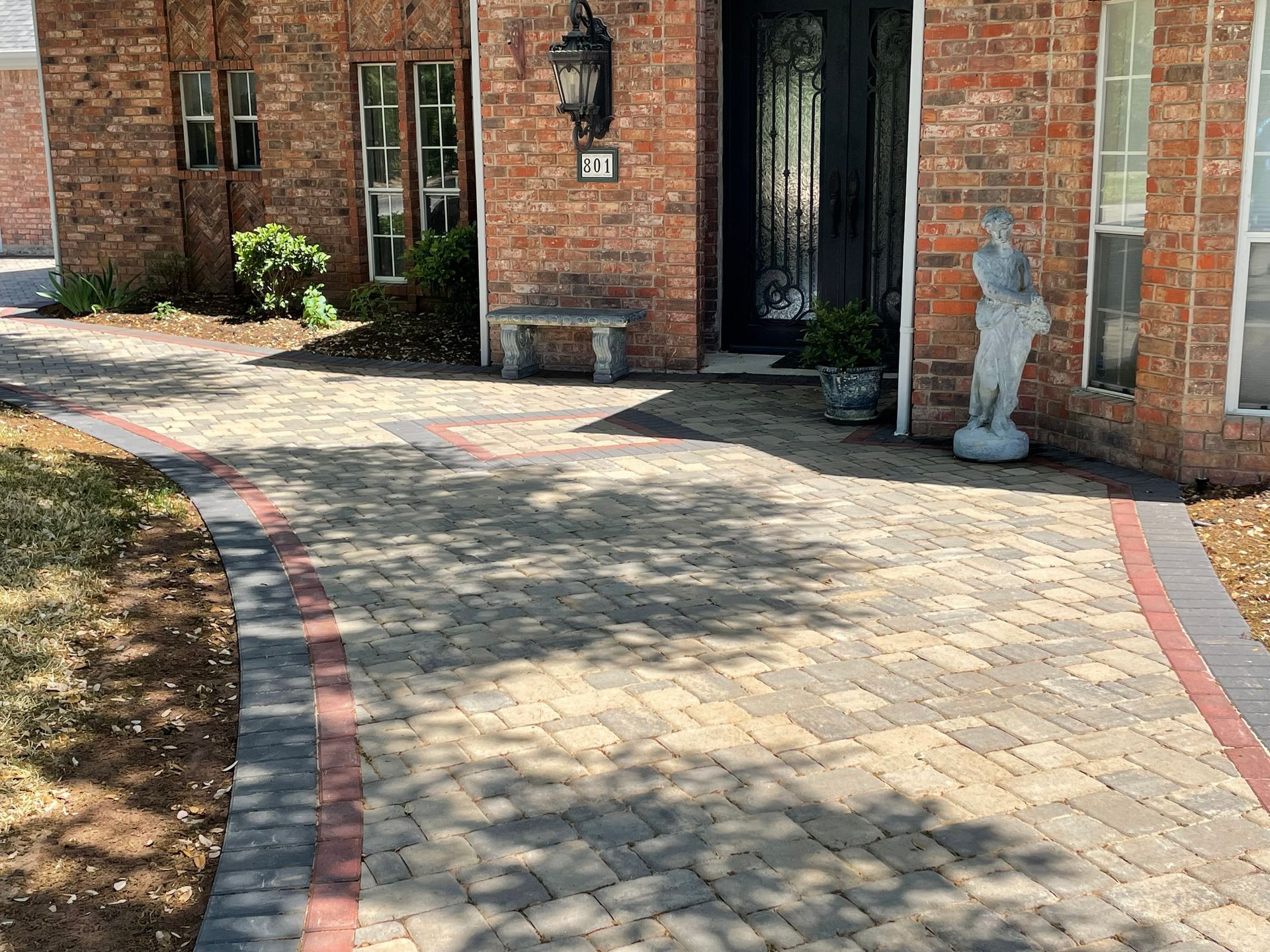 A paved brick walkway leading to a house entrance with a stone bench and a garden statue.