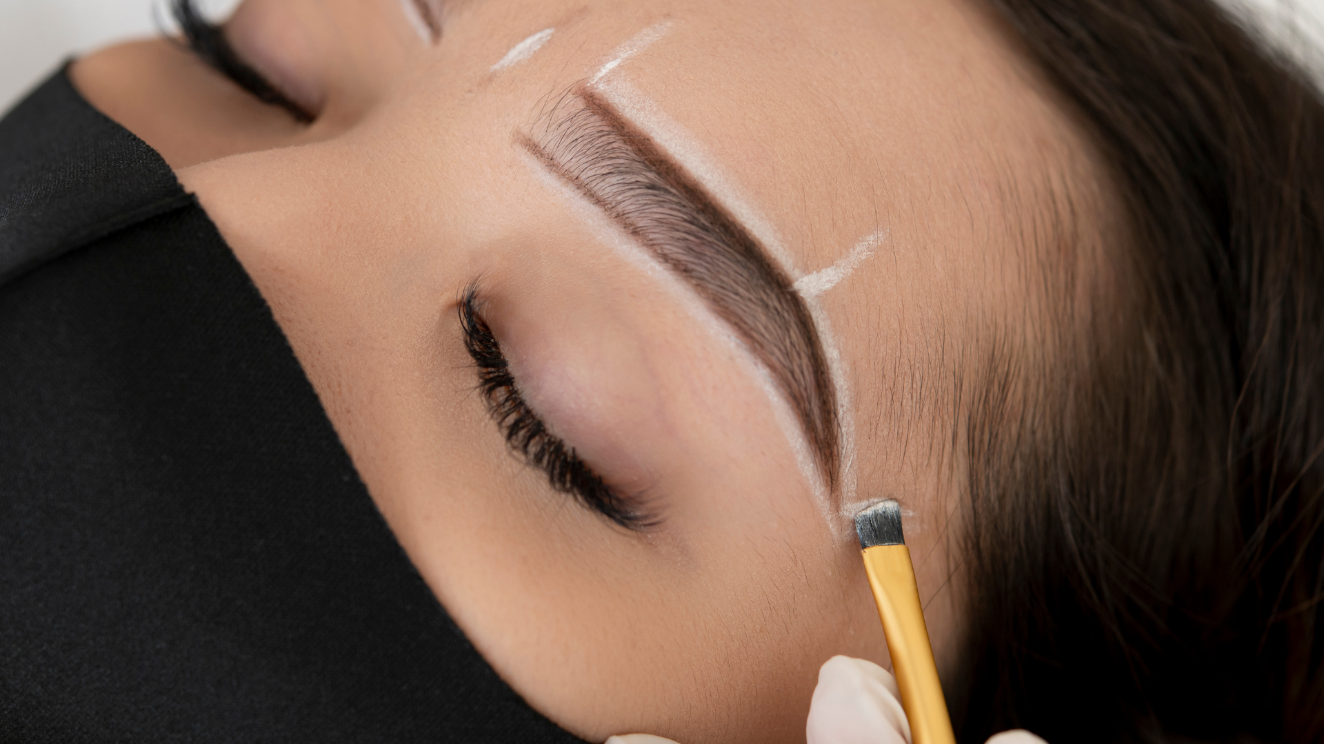 A woman is getting her eyebrows painted with a brush.