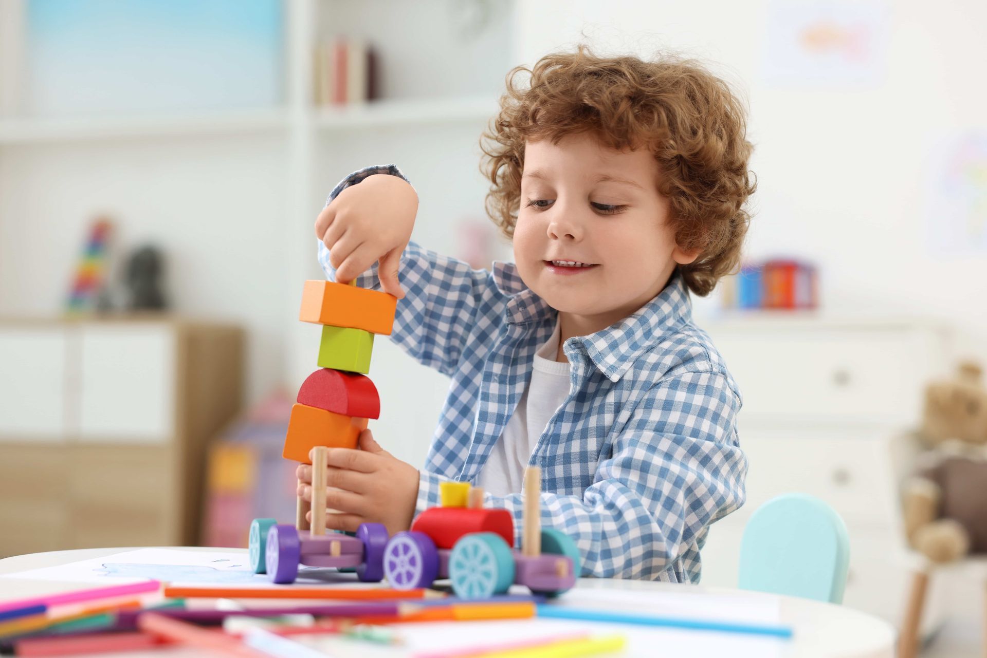 Boy with curly hair stacking colorful wooden blocks on a table.