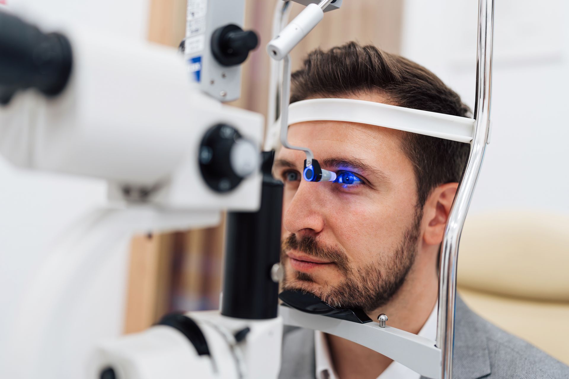 Man at an eye exam using a phoropter, with blue light reflecting in his eyes Man at an eye exam using a phoropter, with blue light reflecting in his eyes