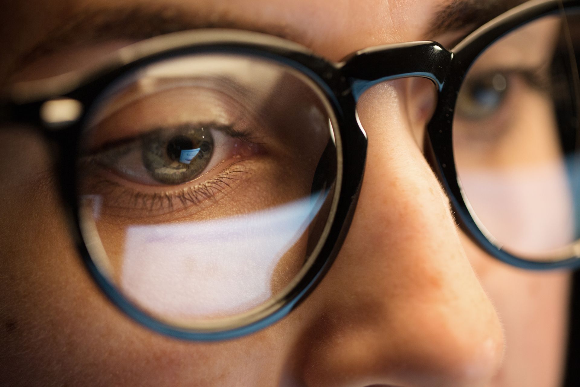 Close-up of a person wearing black glasses, with a reflection visible in the lens