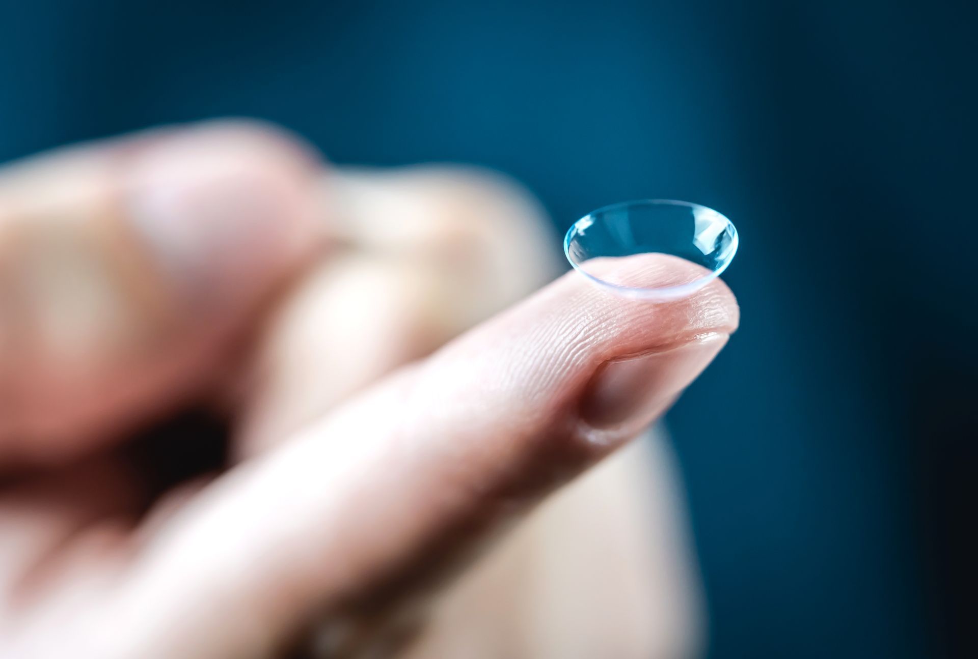 Hand holding a clear contact lens against a blue background Hand holding a clear contact lens against a blue background