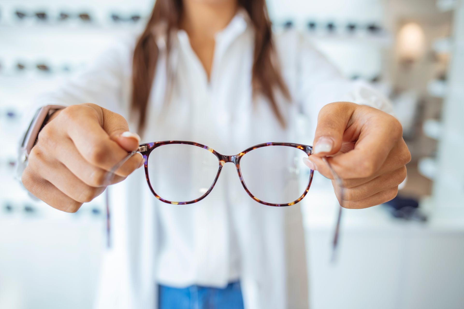 Hands holding round tortoiseshell eyeglasses in front of a blurred person in a white coat Hands holding round tortoiseshell eyeglasses in front of a blurred person in a white coat