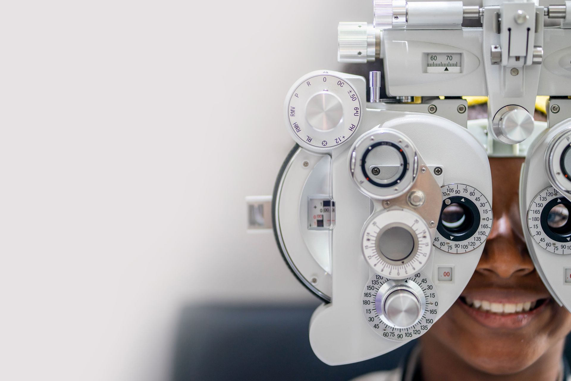 Person smiling during an eye exam with a phoropter in front of their face