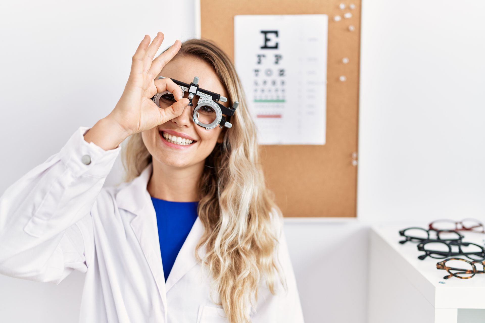 Optometrist holding eyeglasses in an eye exam room, with vision chart and frames on display