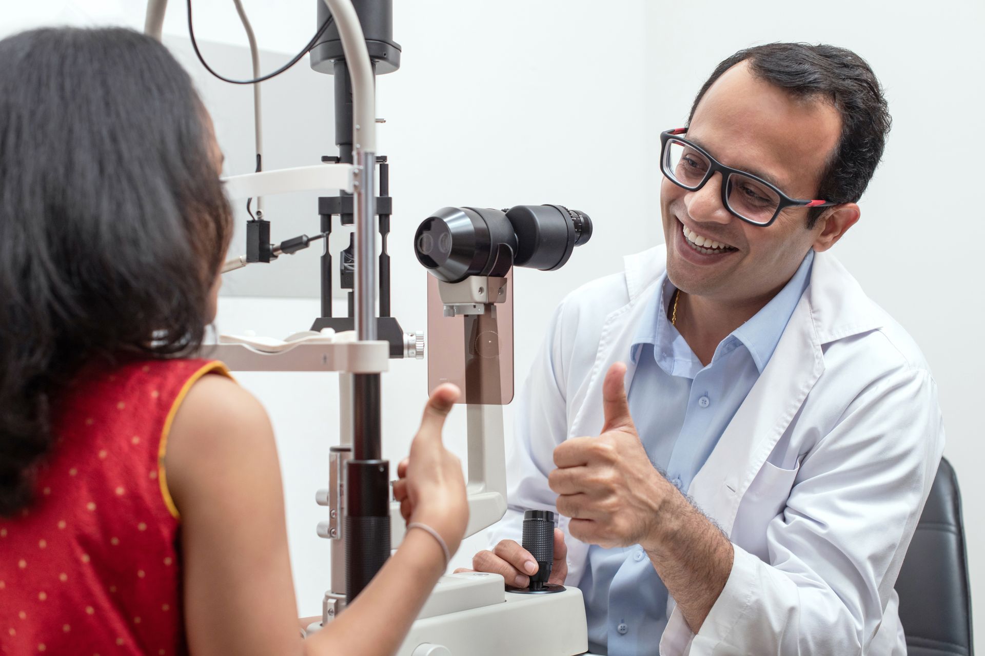 Eye doctor examining a patient at a slit lamp in a clinic, smiling and speaking with her. Eye doctor examining a patient at a slit lamp in a practice, smiling and speaking with her.