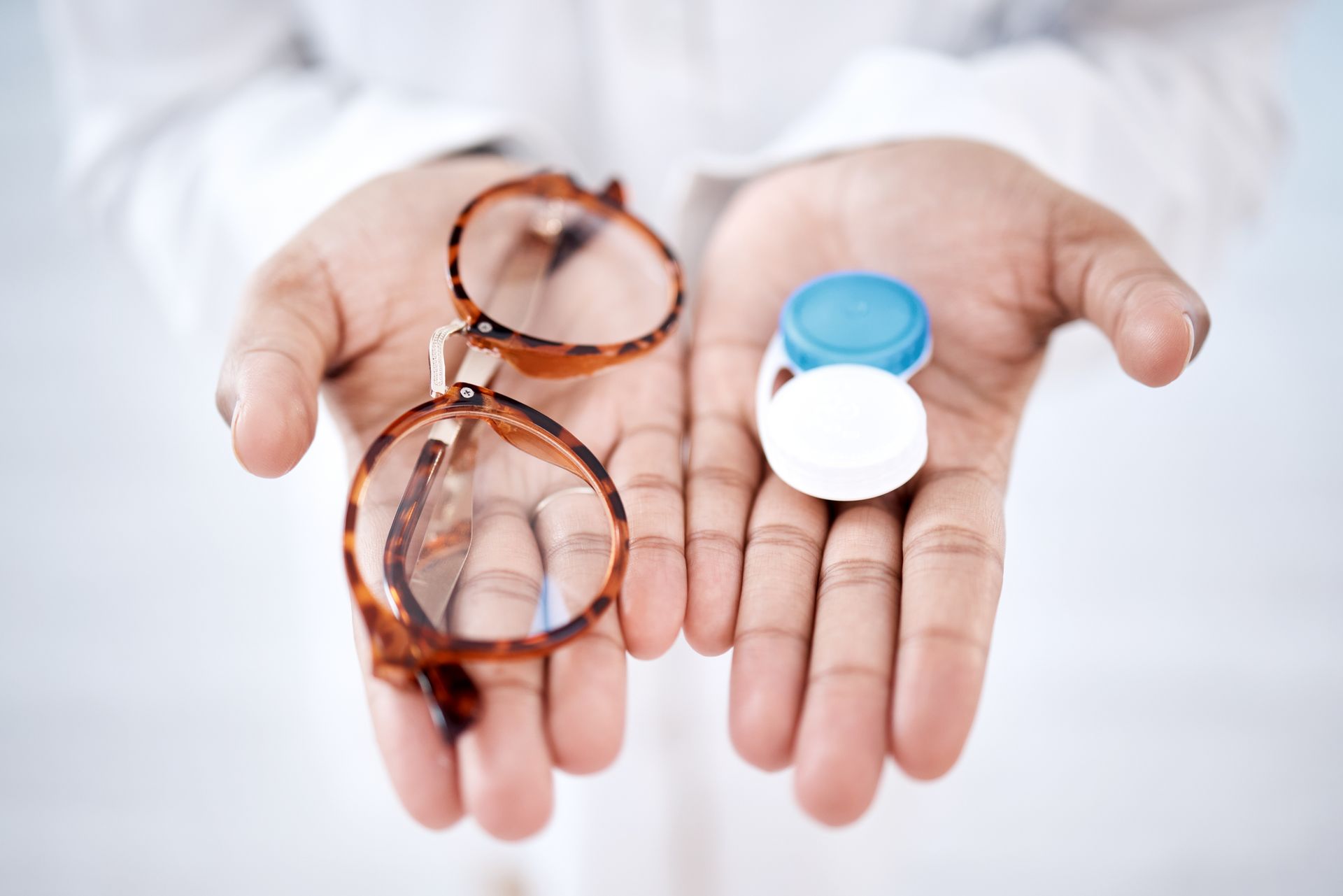 Hands holding eyeglasses and two contact lenses, one blue and one white, on a white background Hands holding eyeglasses and two contact lenses, one blue and one white, on a white background