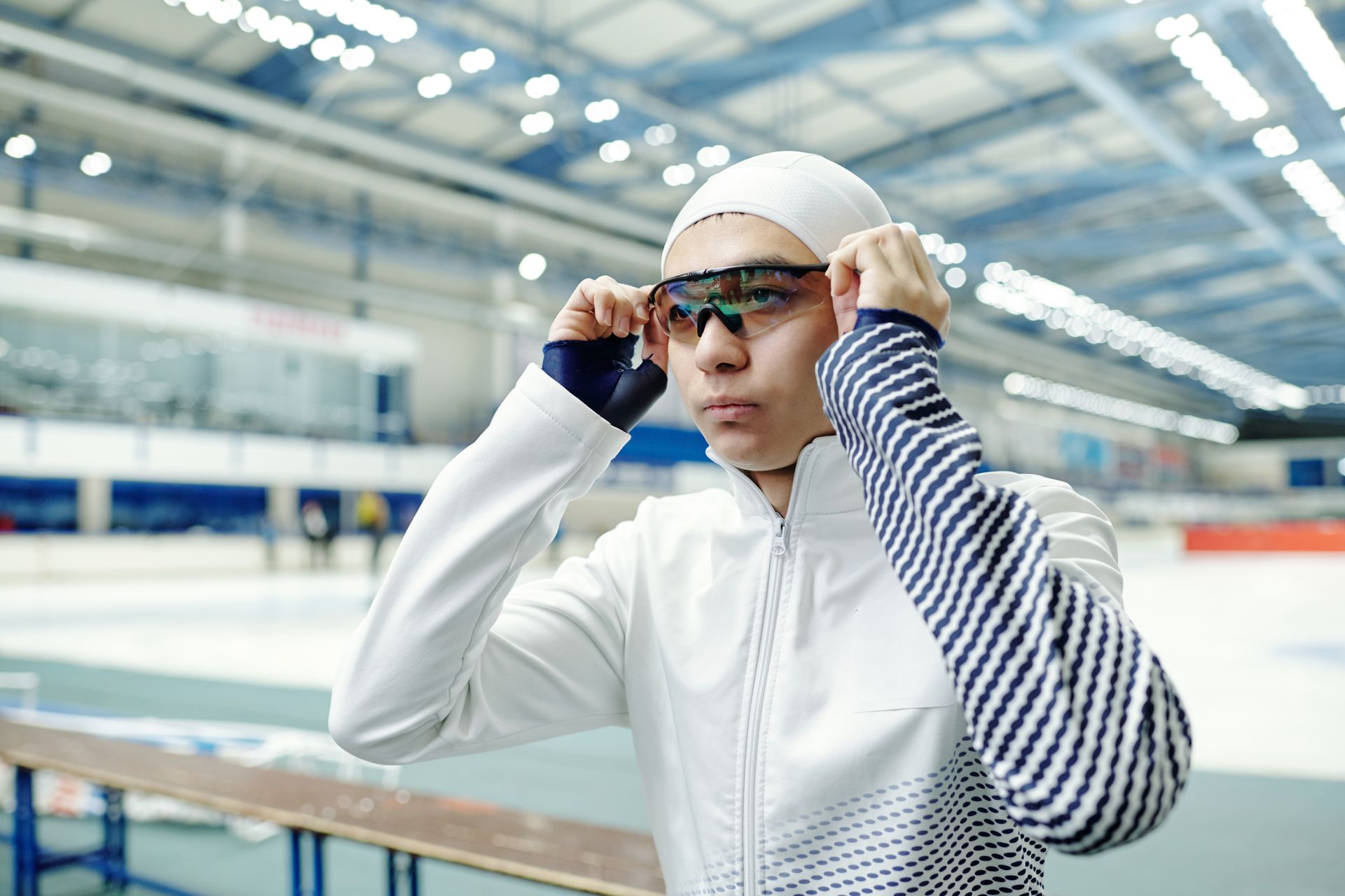Swimmer adjusting goggles at an indoor pool, wearing a white suit and striped sleeves Swimmer adjusting goggles at an indoor pool, wearing a white suit and striped sleeves