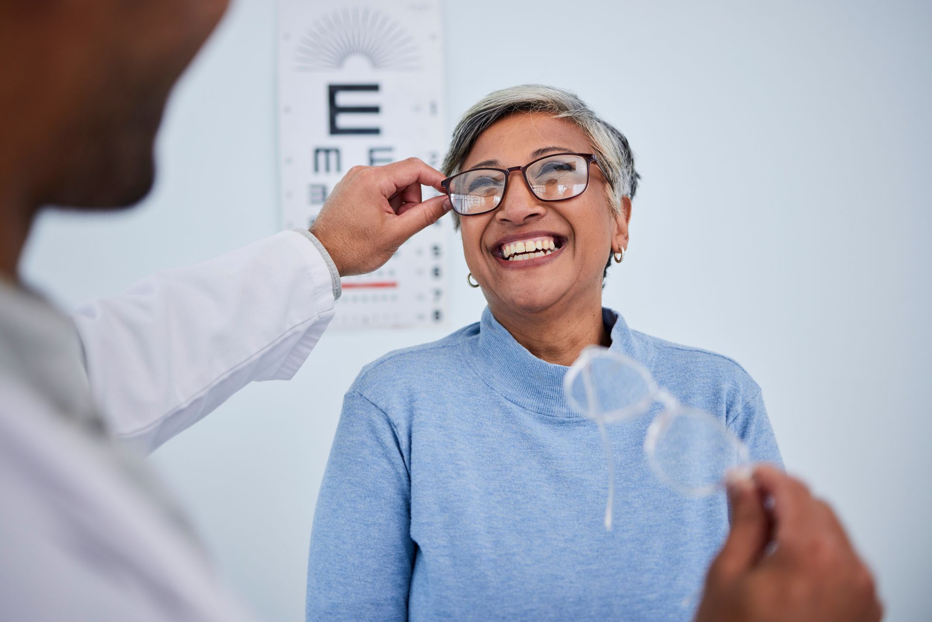 Eye exam with optometrist adjusting glasses on a smiling patient in a clinic Eye exam with optometrist adjusting glasses on a smiling patient in a practice