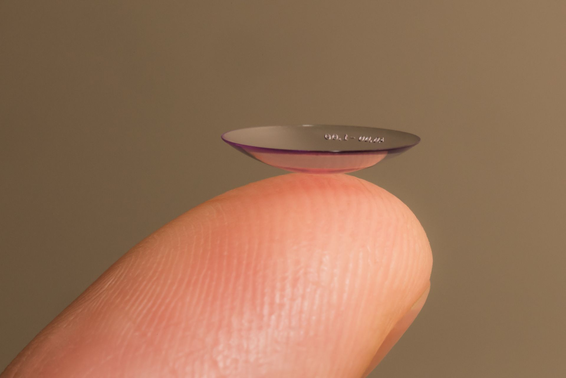 Tiny contact lens balanced on a fingertip against a plain brown background Tiny contact lens balanced on a fingertip against a plain brown background