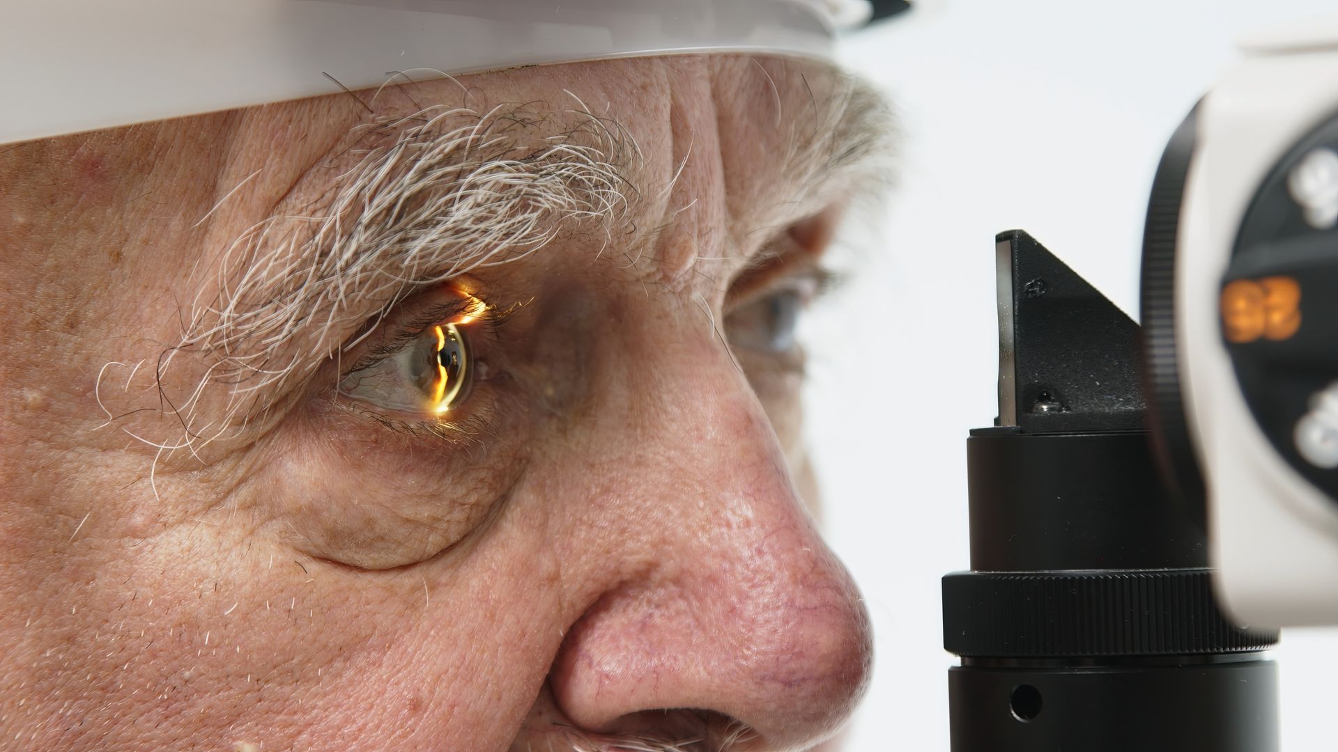 Close-up of a person examining an eye test device, with a bright reflection in the eye