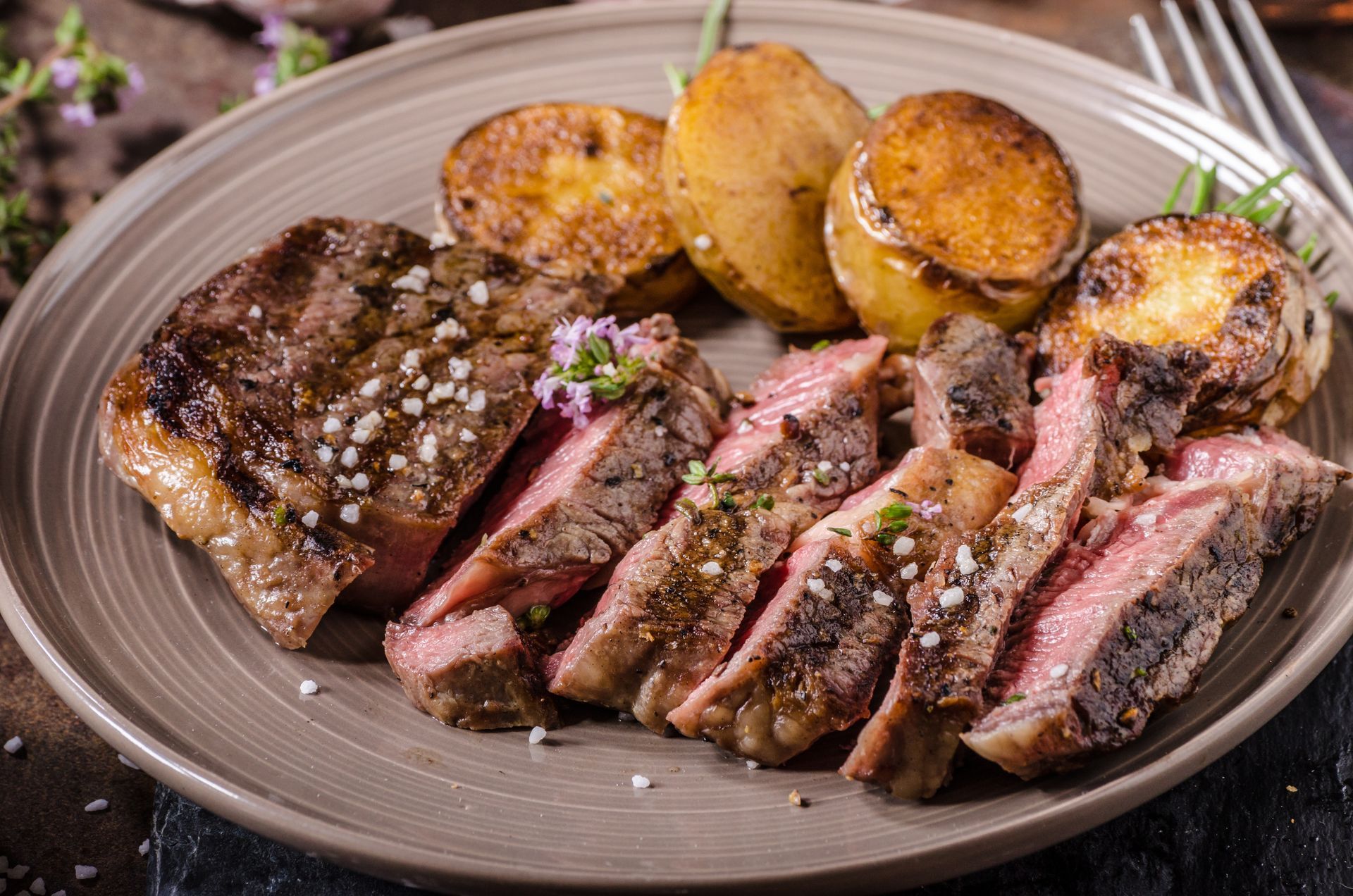 Sliced steak on a plate with roasted potato wedges and seasoning