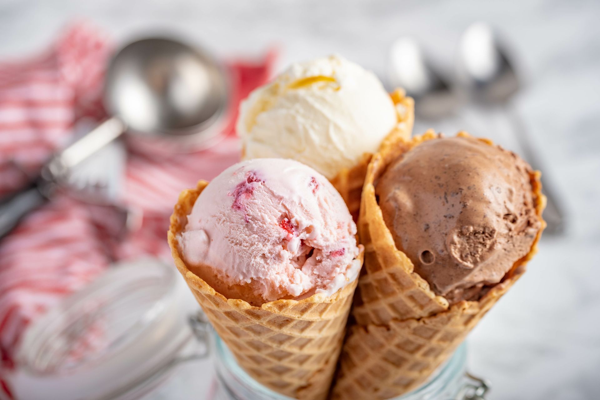Three ice cream cones with pink, vanilla, and chocolate scoops on a table