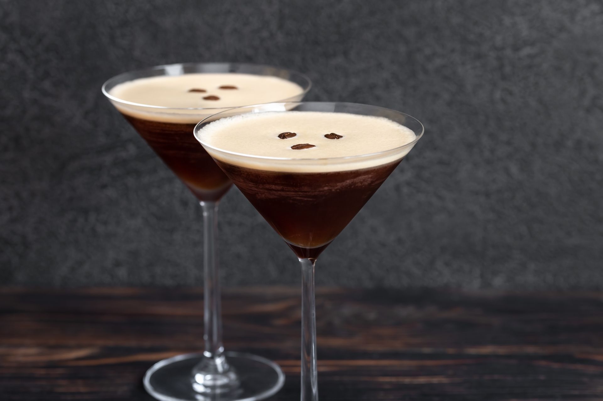 Two creamy espresso martini cocktails in stemmed glasses on a dark tabletop