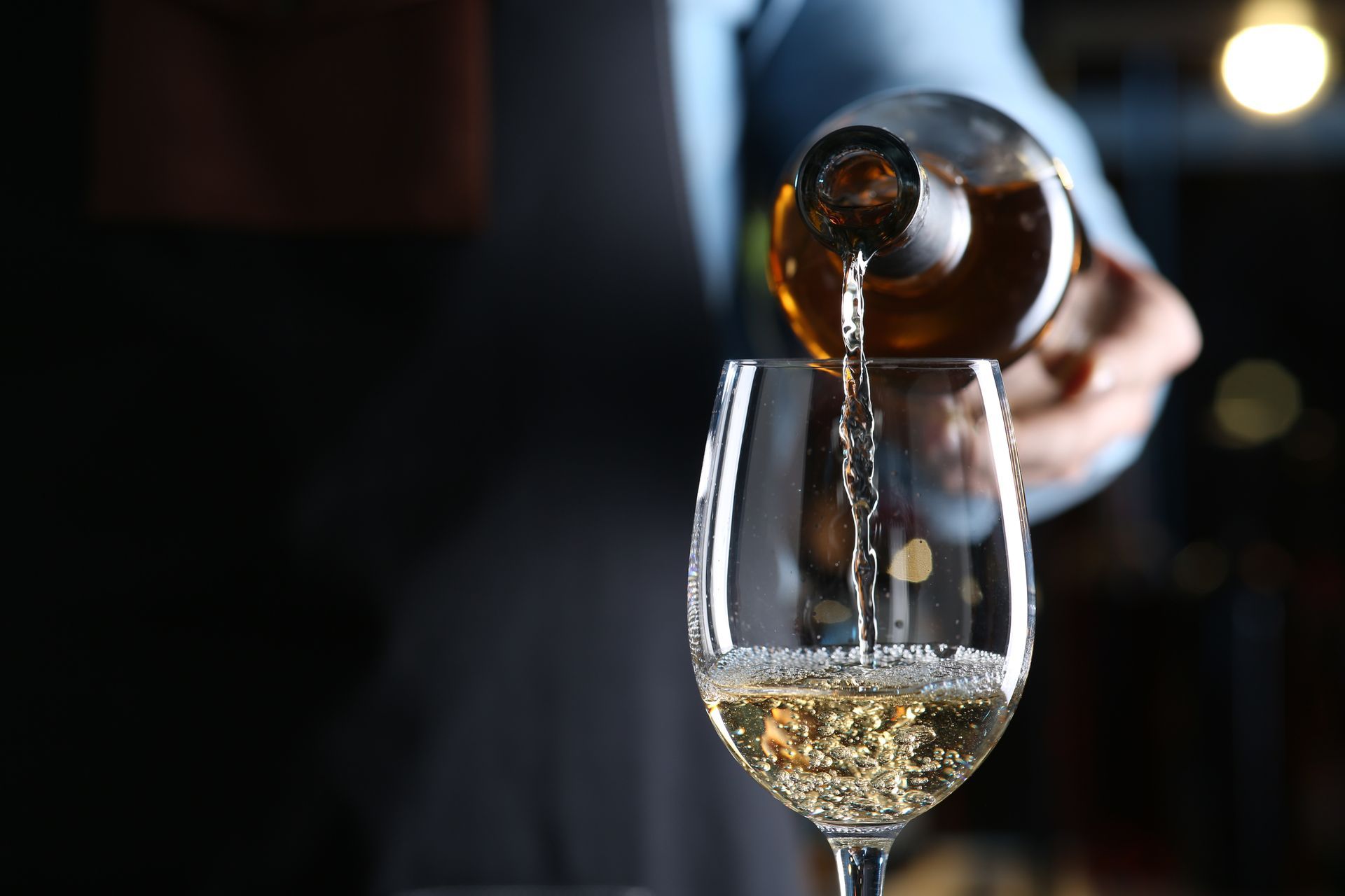 Wine being poured into a glass from a bottle in a dimly lit setting