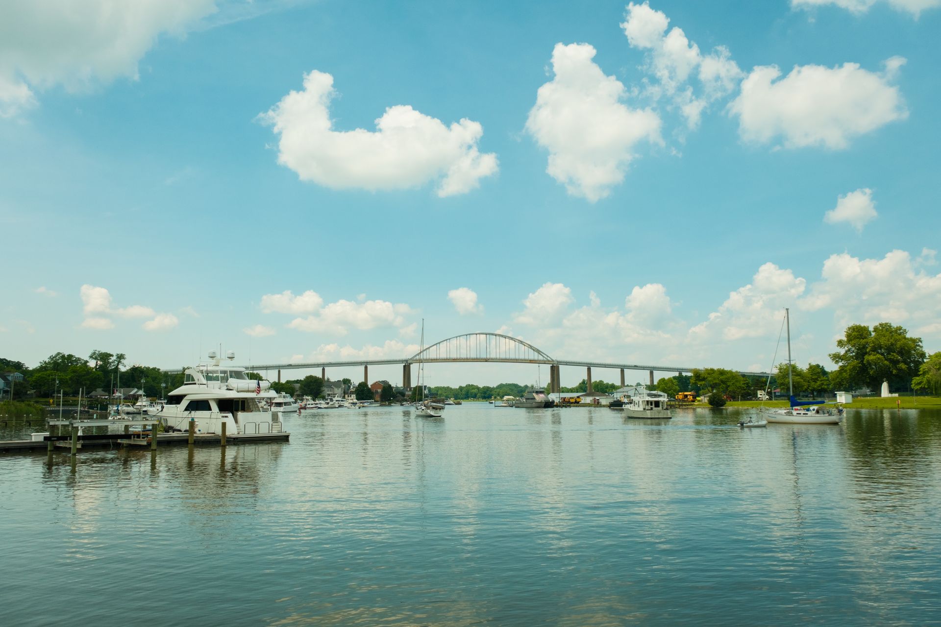 Riverfront marina with boats, a bridge in the distance, and a calm blue sky reflected on the water