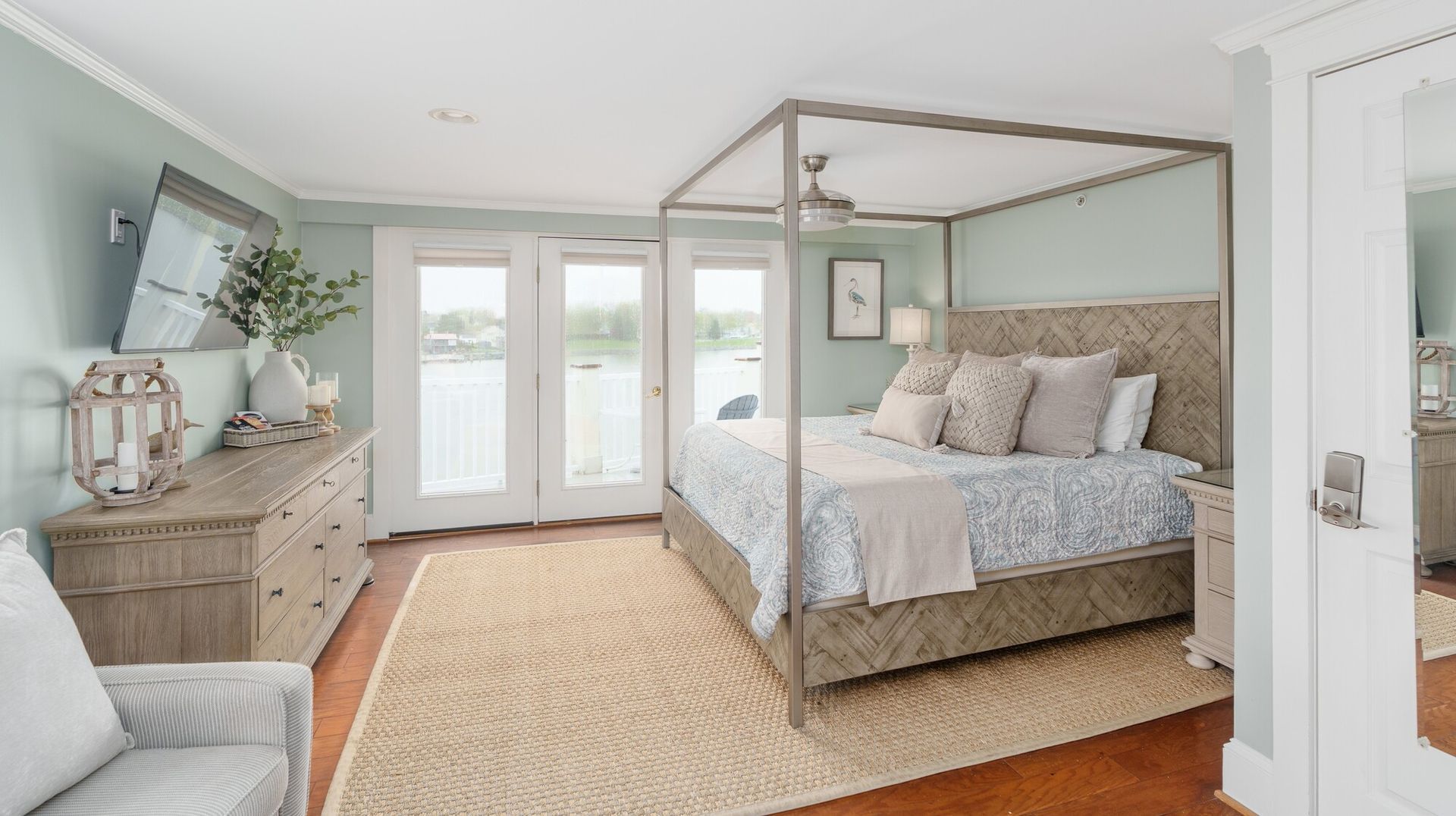 Bright bedroom with a canopy bed, dresser, rug, and French doors opening to a patio.