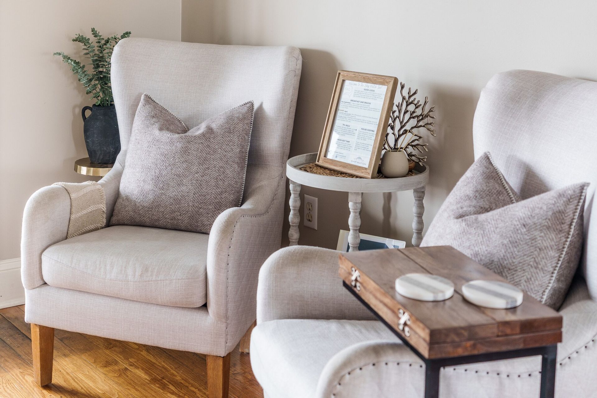 Cozy living room with two beige armchairs, a side table, and a wooden tray on a white chair.