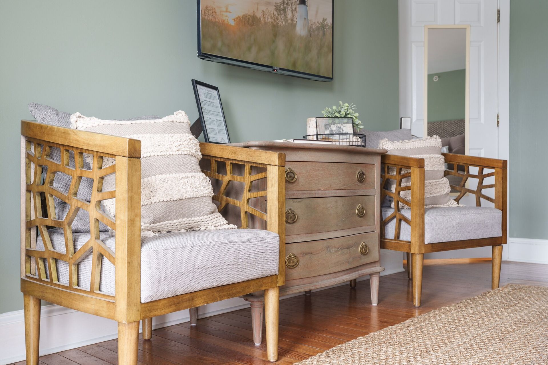Cozy living room seating with two wooden armchairs, a side cabinet, and a wall-mounted TV in neutral tones
