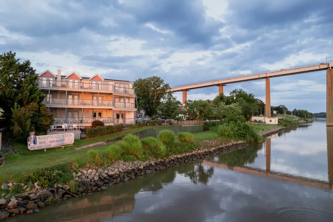 Canal-side building and bridge reflected in calm water under a cloudy sky