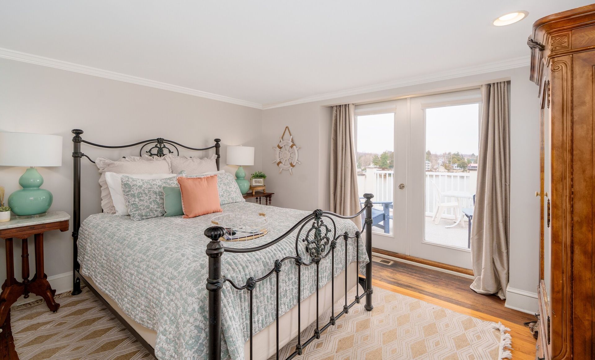 Bright bedroom with wrought-iron bed, pastel bedding, and French doors opening to a balcony