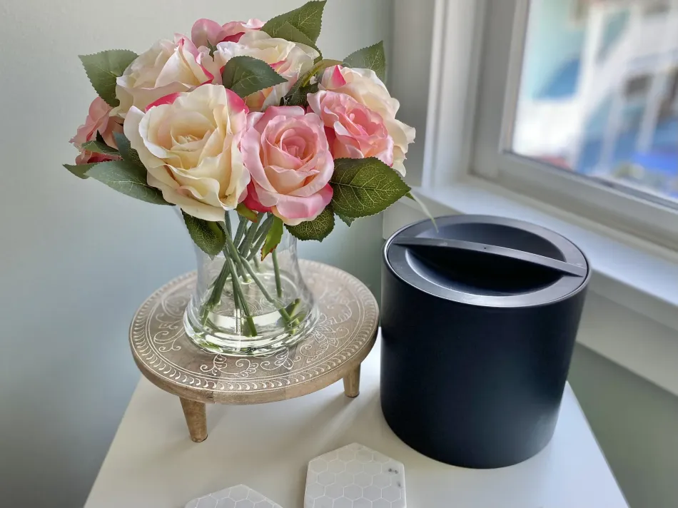 Pink and cream roses in a glass vase on a small table beside a black candle holder by a window