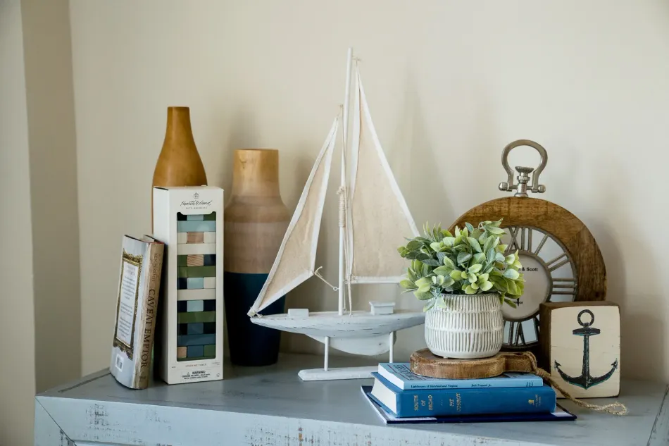 Decorative shelf with a white model sailboat, books, jars, and woven home decor accents