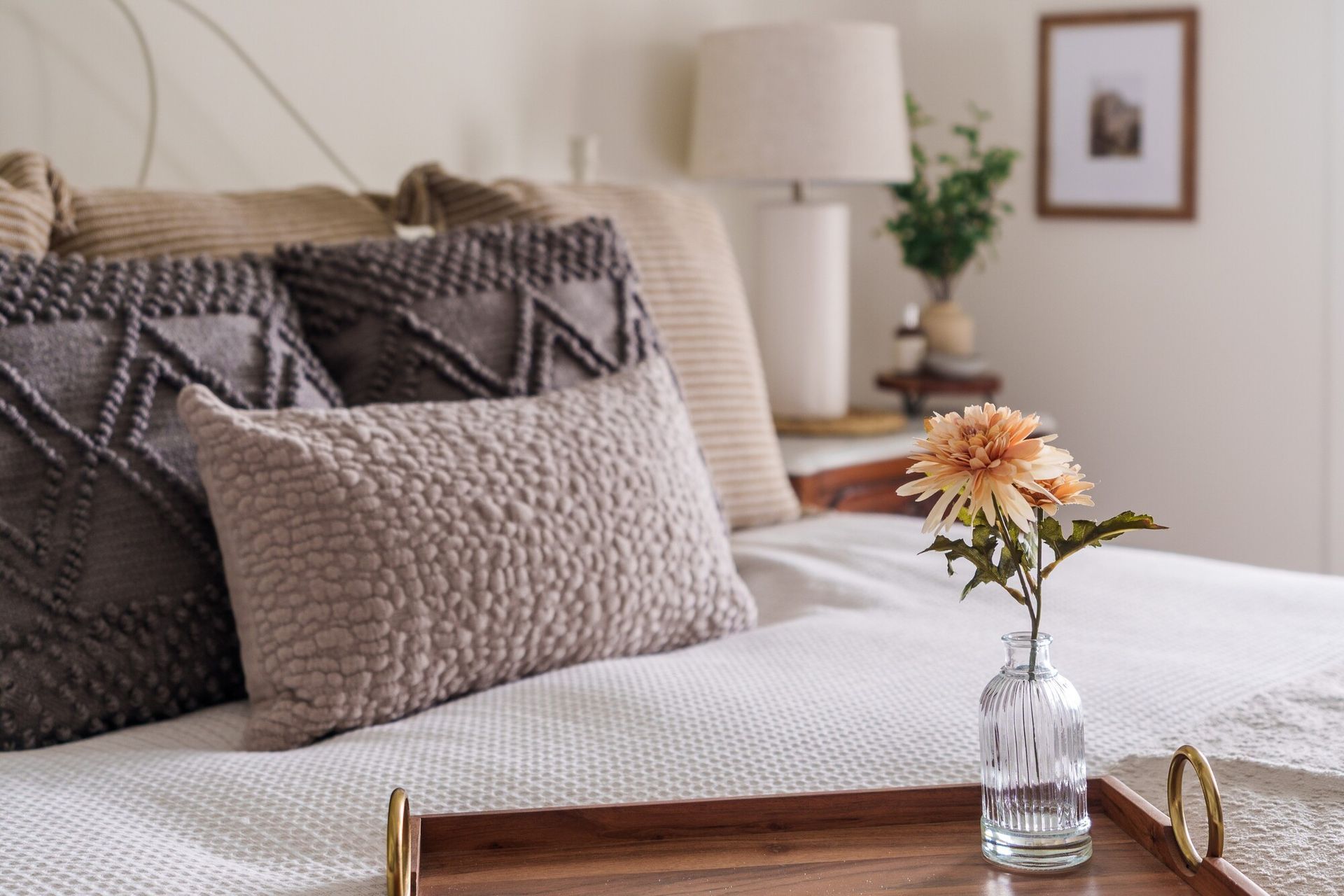 Cozy bedroom with layered pillows, a white bedspread, and a small flower vase on a tray table