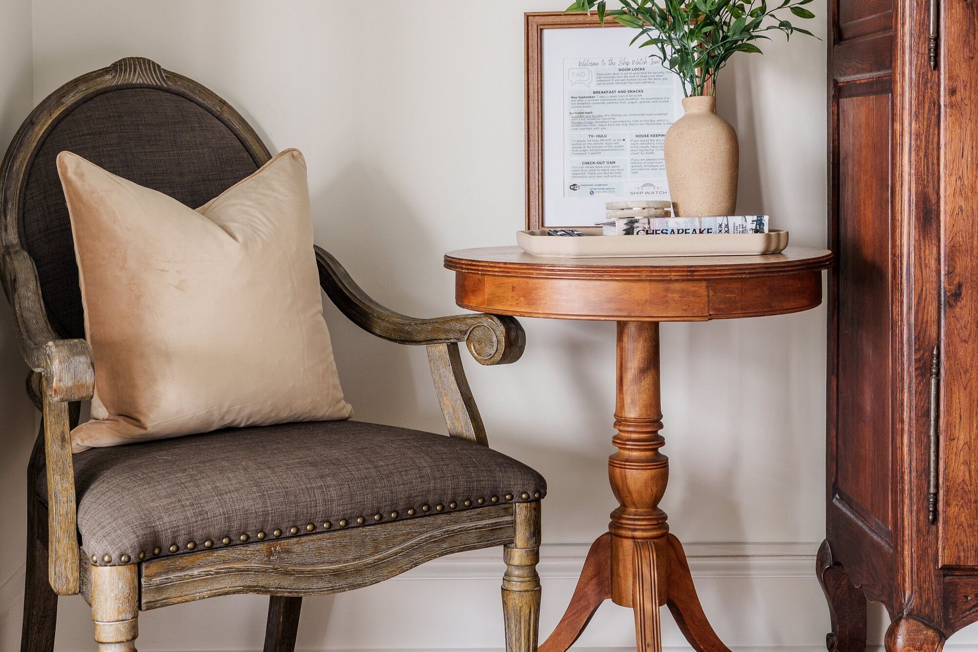 Vintage chair with beige pillow beside a small round wooden table and framed decor