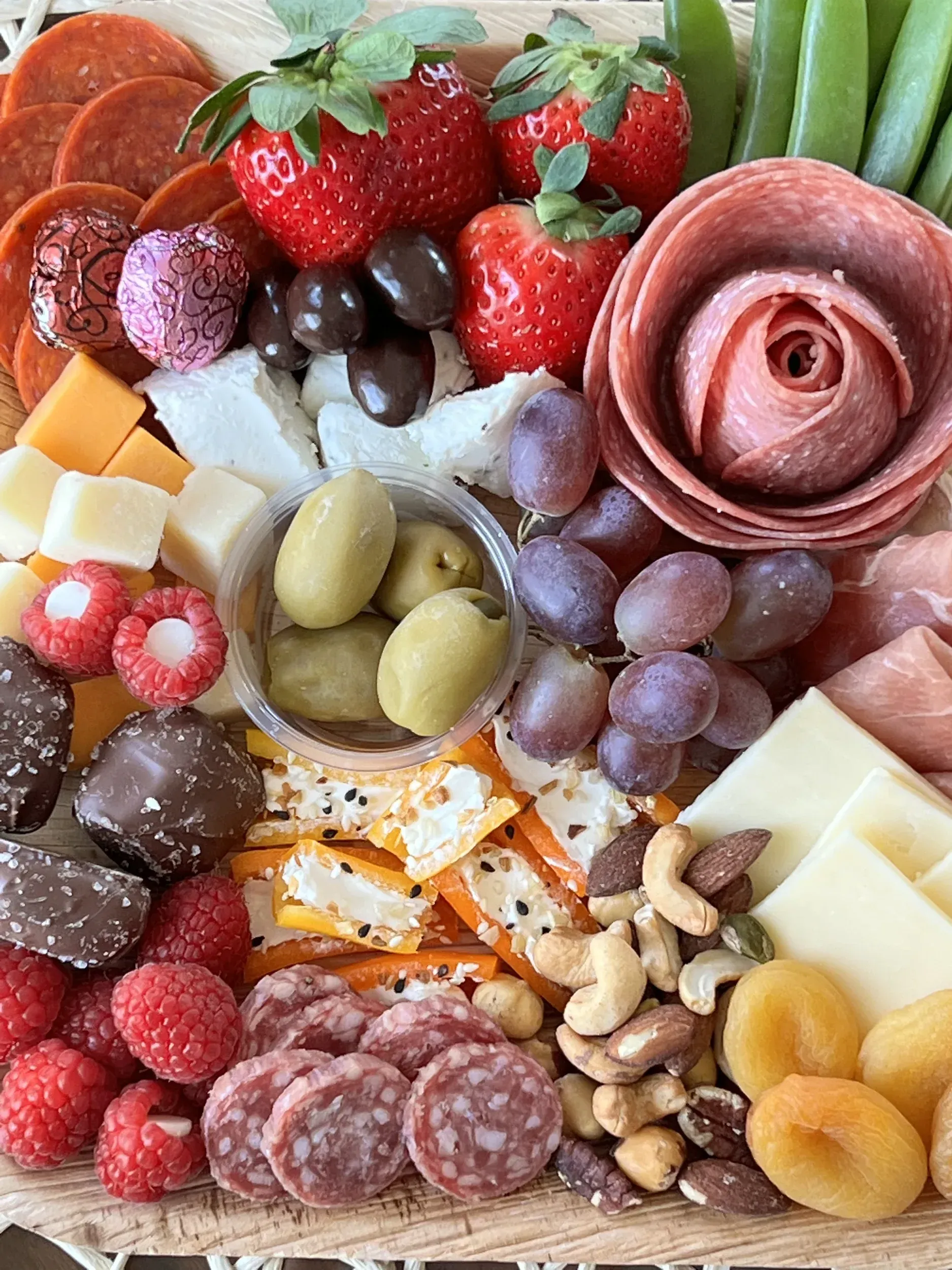 Charcuterie board with strawberries, grapes, cheeses, meats, nuts, olives, and crackers arranged in a flower shape