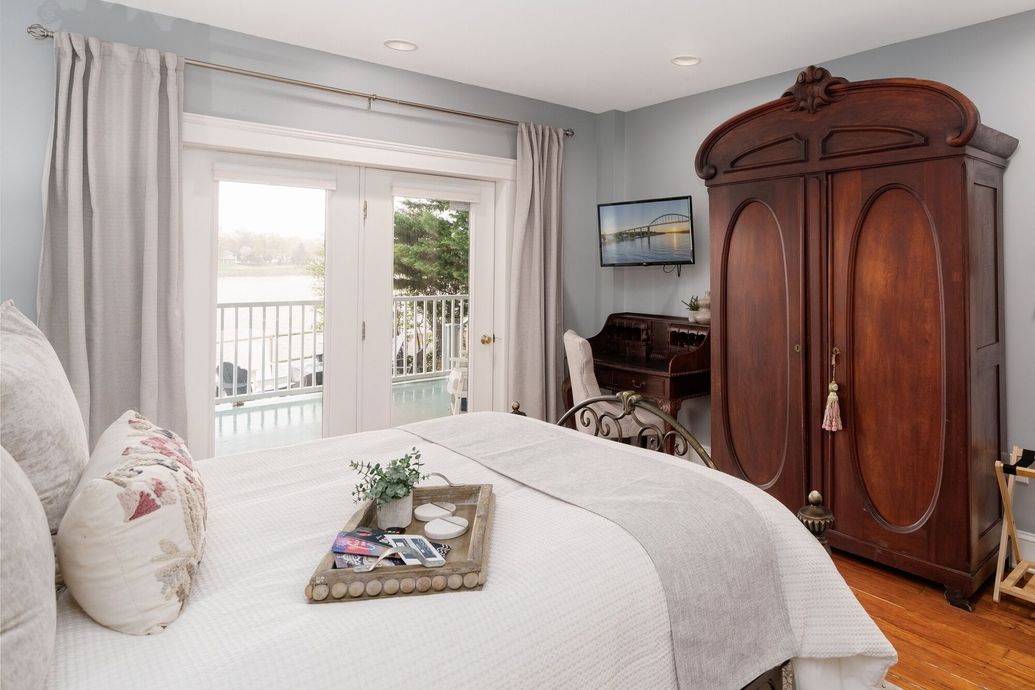 Bright bedroom with white bed, French doors, and a large wooden armoire