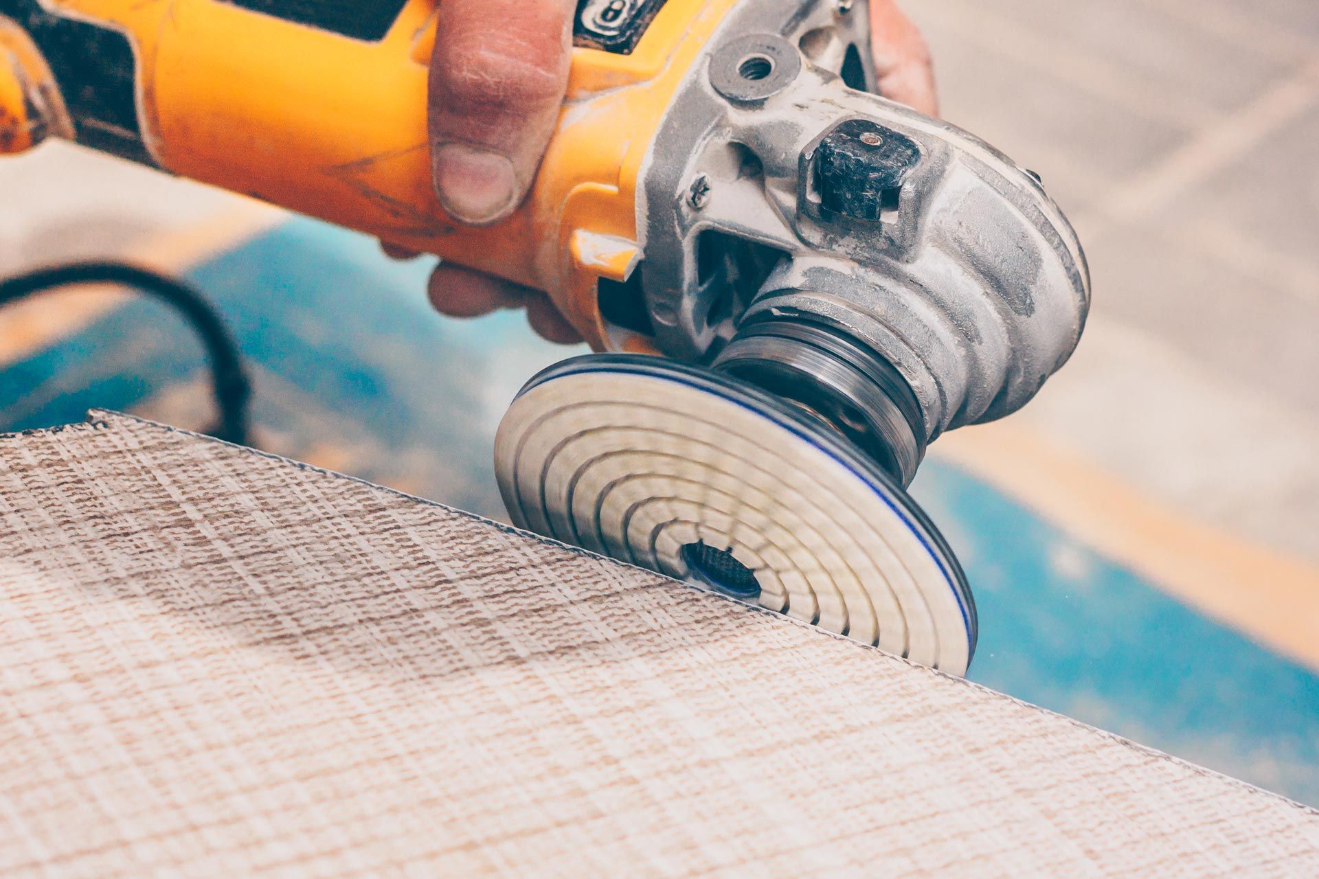 Worker using angle grinder with polishing disc to cut or grind ceramic tile on job site.
