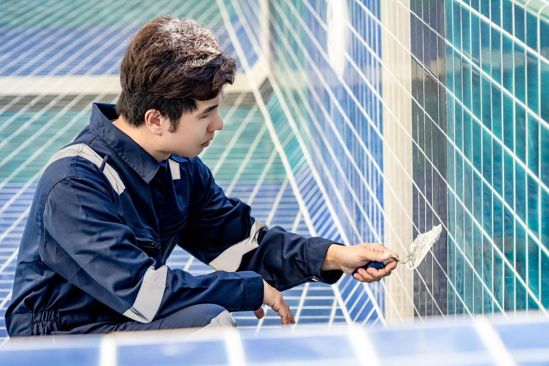 Worker applying grout to blue ceramic tiles during pool remodeling.