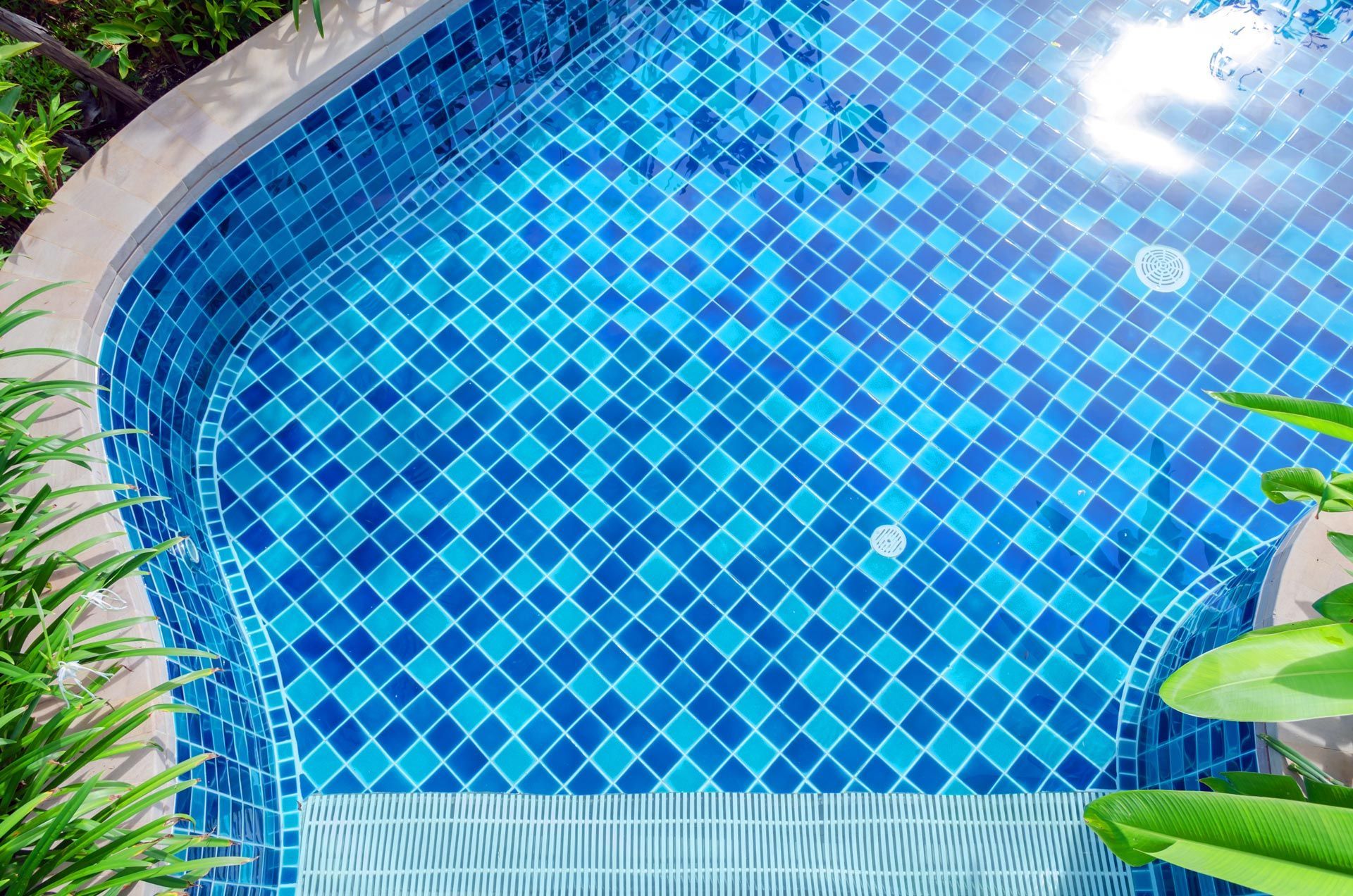 A clear swimming pool with blue mosaic tiles viewed from above, showing clean lines and calm water. A clear swimming pool with blue mosaic tiles viewed from above, showing clean lines and calm water.