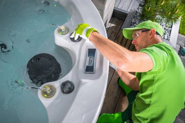 Hot tub technician in green uniform inspecting and servicing outdoor spa jets and controls.