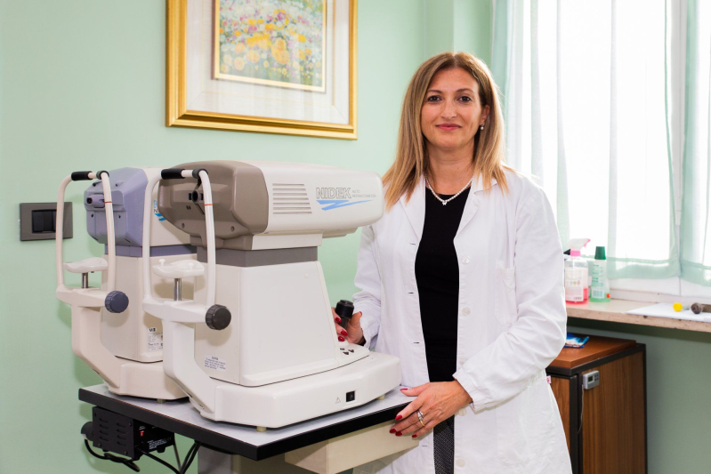 Un medico in piedi accanto a un apparecchio per esami oculistici in una stanza della clinica.